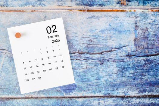 February 2023 monthly calendar and wooden push pin on blue wooden background.
