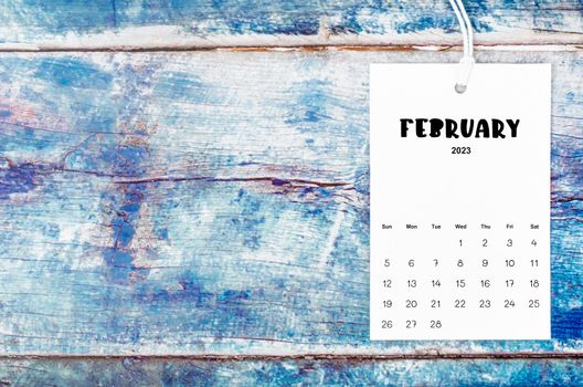 February 2023 calendar page hanged with white rope on old blue wooden background.