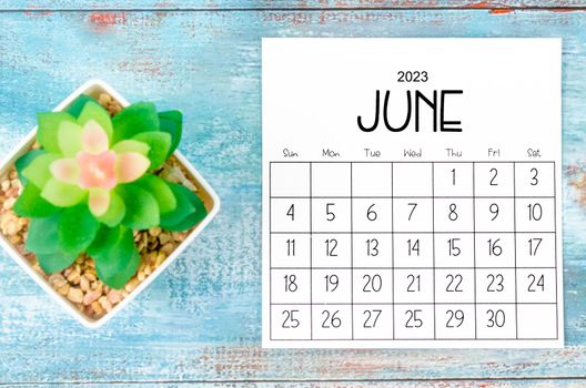 June 2023 Monthly calendar with plant pot on wooden background.