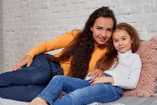 Love of young mother and daughter. They lie on the bed at home and have fun, they feel good.