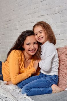 Love of young mother and daughter. They sit on the bed at home and have fun, they hold each other and show their emotions