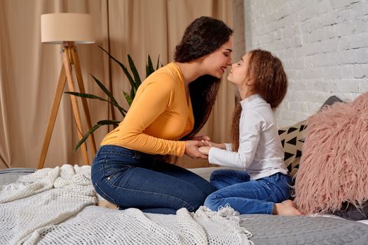 Love of young mother and daughter. They sit on the bed at home and have fun, they hold each other and show their emotions