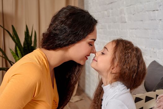 Love of young mother and daughter. They sit on the bed at home and have fun, they hold each other and show their emotions