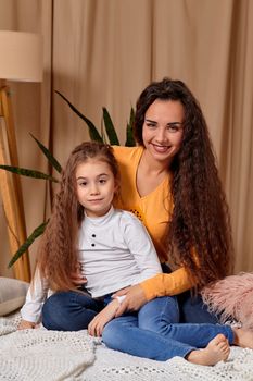 Love of young mother and daughter. They sit on the bed at home and have fun, mother hugs daughter