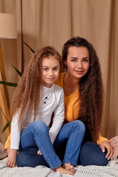 Love of young mother and daughter. They sit on the bed at home and have fun, mother hugs daughter