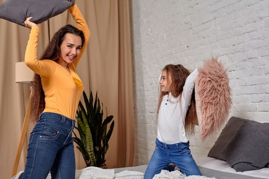 mom and daughter sit on bed, fooling around with pillow fights, they have fun, they looks happy