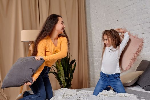 mom and daughter sit on bed, fooling around with pillow fights, they have fun, they looks happy