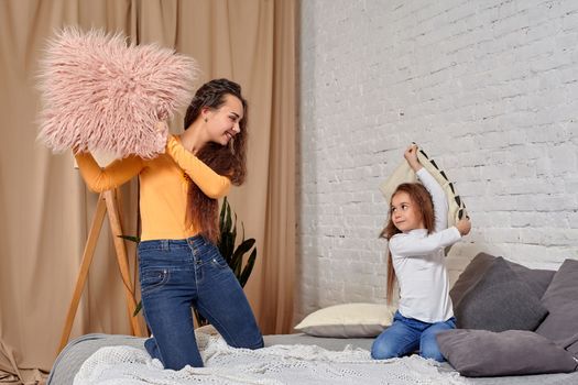 mom and daughter sit on bed, fooling around with pillow fights, they have fun, they looks happy