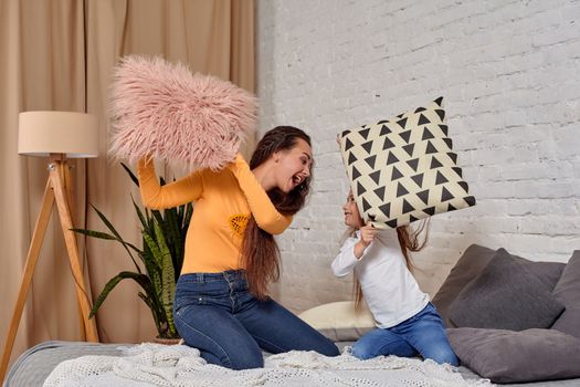 mom and daughter sit on bed, fooling around with pillow fights, they have fun, they looks happy