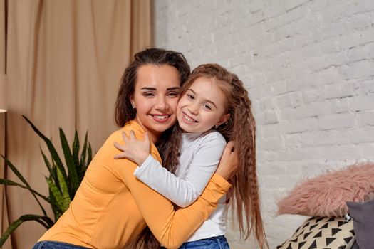 Love of young mother and daughter. They sit on the bed at home and have fun, they hold each other and show their emotions