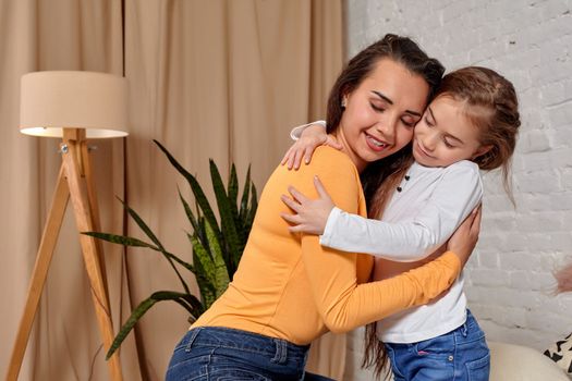 Love of young mother and daughter. They sit on the bed at home and have fun, they hold each other and show their emotions