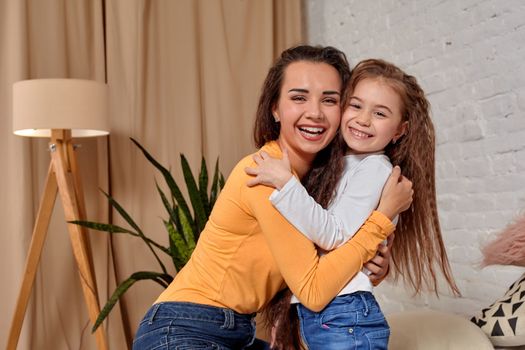 Love of young mother and daughter. They sit on the bed at home and have fun, they hold each other and show their emotions