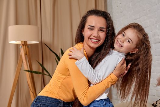 Love of young mother and daughter. They sit on the bed at home and have fun, they hold each other and show their emotions