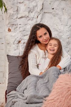 Mother and daughter sitting on sill near window in room. They show emotions and have fun