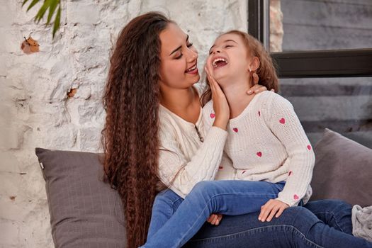 Mother and daughter sitting on sill near window in room. They show emotions and have fun