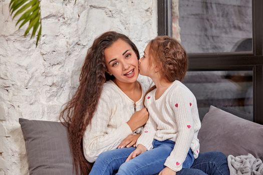 Mother and daughter sitting on sill near window in room. They show emotions and have fun