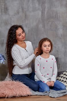 Eemotions of a beautiful young mother and her little daughter who spend time together. They sit on the floor and mom cares for her daughter's hair