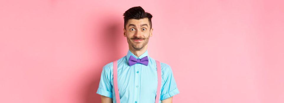 Smiling caucasian man looking excited, standing in classy bow-tie and shirt for romantic date, pink background.