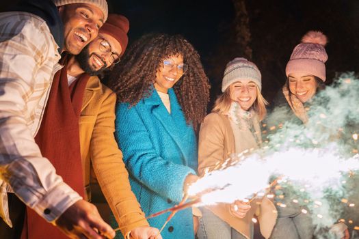 Happy friends enjoying outdoors with sparklers - Group of young people cheerful celebrating with fireworks - Holidays and friendship concept