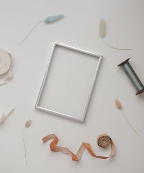 minimal mockup with blank frame with sewing thread and sewing items on white background, flatlay, top view, copy space.
