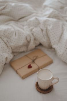 Cup of coffee with milk and gift box in bed with plaid, copy space. Flat lay, top view. morning in bed concept composition. 