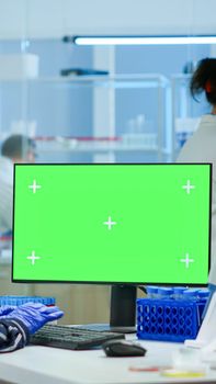 Medical research scientist working on pc with green screen mock up template in applied science laboratory. Engineers conducting experiments in background, examining vaccine evolution using high tech