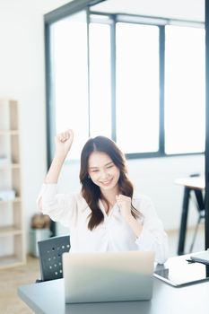 Portrait of a woman business owner showing a happy smiling face as he has successfully invested her business using computers and financial budget documents at work.