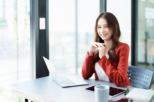 Portrait of a woman business owner showing a happy smiling face as he has successfully invested her business using computers and financial budget documents at work.