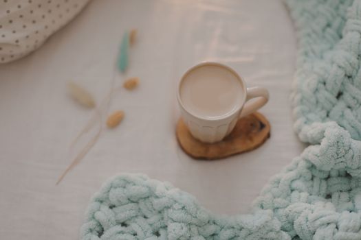 Cup of coffee with milk on the bed with white linens and blanket. Morning coffee in bed concept