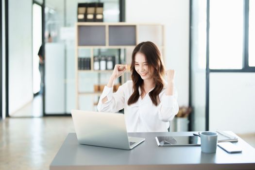 Portrait of a woman business owner showing a happy smiling face as he has successfully invested her business using computers and financial budget documents at work.