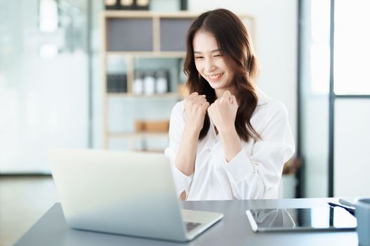 Portrait of a woman business owner showing a happy smiling face as he has successfully invested her business using computers and financial budget documents at work.