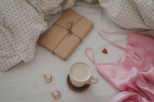 Cup of coffee with milk and gift box in bed with plaid, copy space. Flat lay, top view. morning in bed concept composition. 