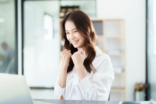 Portrait of a woman business owner showing a happy smiling face as he has successfully invested her business using computers and financial budget documents at work.