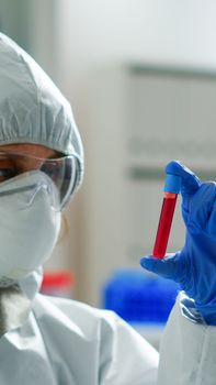 Biochemist in coverall holding blood sample analysing chemical reaction working in medical lab. Scientist examining vaccine evolution using high tech for treatment development against covid19 virus