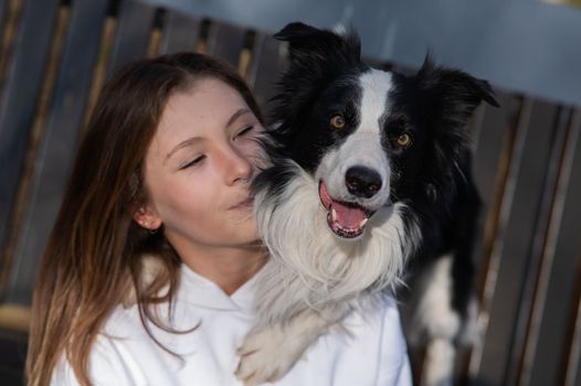 Caucasian woman hugging her dog Border Collie while sitting on a bench in autumn park