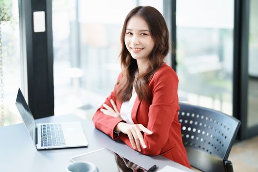 Portrait of a woman business owner showing a happy smiling face as he has successfully invested her business using computers and financial budget documents at work.