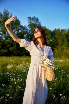 a beautiful woman in a light summer dress stands in nature and closes her hand from the rays of the sun. High quality photo