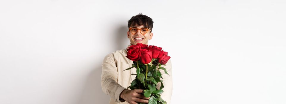 Handsome boyfriend giving you bouquet of roses, make surprise gift on romantic date at valentines day, standing with lover over white background.