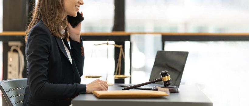 Lawyer woman talking mobile phone and working on tablet and laptop on table in office...