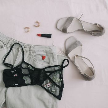 Overhead view of woman's casual spring summer outfit with jeans, sandals and red lipstick on beige background, Flat lay, top view. 