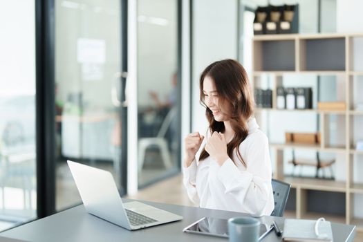 Portrait of a woman business owner showing a happy smiling face as he has successfully invested her business using computers and financial budget documents at work.