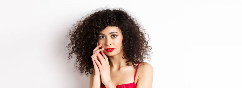 Close-up of tender romantic woman, gently touching face and looking sensual at camera, white background.