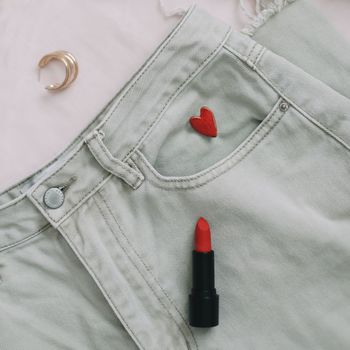 Overhead view of woman's casual outfit with red lipstick and earrings on beige background, Flat lay, top view. 