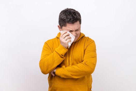 Depressed desperate middle aged man rubbing tired eyes, crying because of hopelessness and loneliness, nervous breakdown, wearing urban style hoodie. Indoor studio shot isolated on white background.