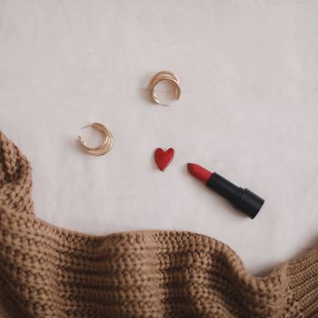 Overhead view of woman's casual outfit with red lipstick and earrings on beige background, Flat lay, top view. 