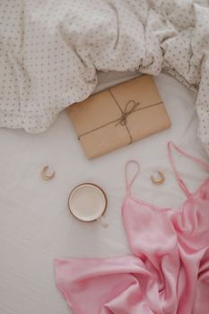 Cup of coffee with milk and gift box in bed with plaid, copy space. Flat lay, top view. morning in bed concept composition. 