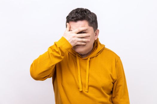 Portrait of handsome man looking through fingers, peeking with curious face, having suspicious, watching secrets, wearing urban style hoodie. Indoor studio shot isolated on white background.