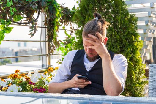 Upset man looking at smartphone holding his head while sitting in penthouse got bad news.