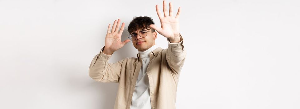 Image of reluctant and annoyed man raising hands up to block offer, refusing and asking to stop, telling no, declining something, standing on white background.