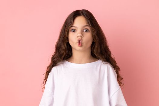 Portrait of excited funny little girl making fish face with lips and big amazed eyes, looking surprised and silly at camera, wondered expression. Indoor studio shot isolated on pink background.